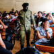 A Ugandan police officer walks past detainees seated in a room after authorities arrested dozens of foreigners in a crackdown on illegal migration, in Kampala, Uganda, Tuesday. | Source: AP